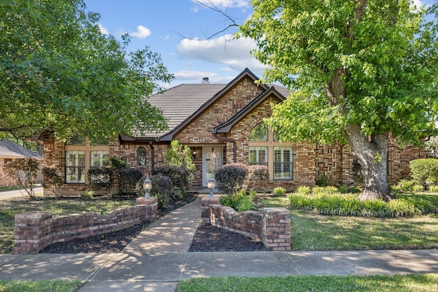 tudor home featuring brick siding, a tile roof, and a chimney