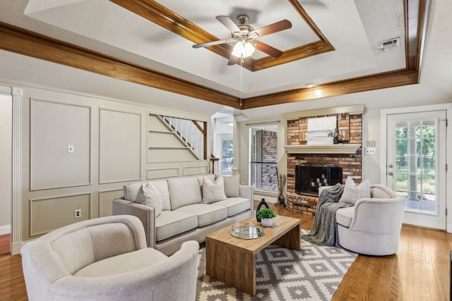 living room featuring a raised ceiling, stairway, light wood-style floors, a ceiling fan, and a fireplace