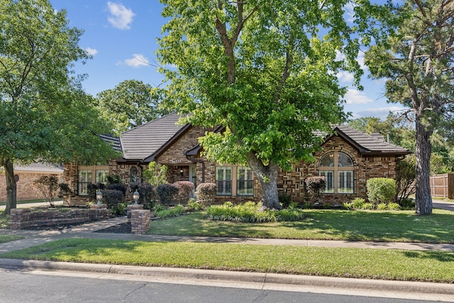 tudor house with a front yard, a tiled roof, brick siding, and stone siding