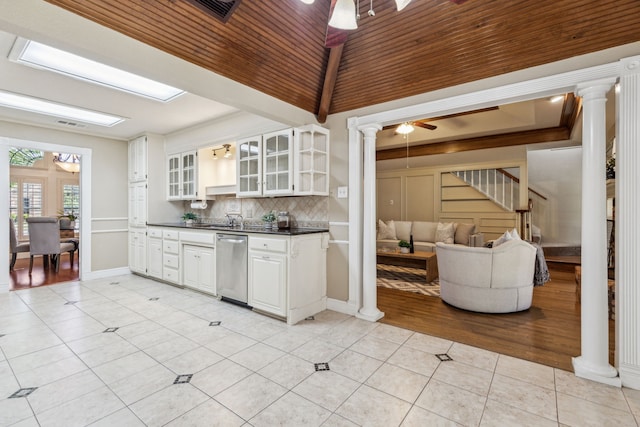 kitchen featuring decorative columns, dark countertops, stainless steel dishwasher, open shelves, and light tile patterned flooring