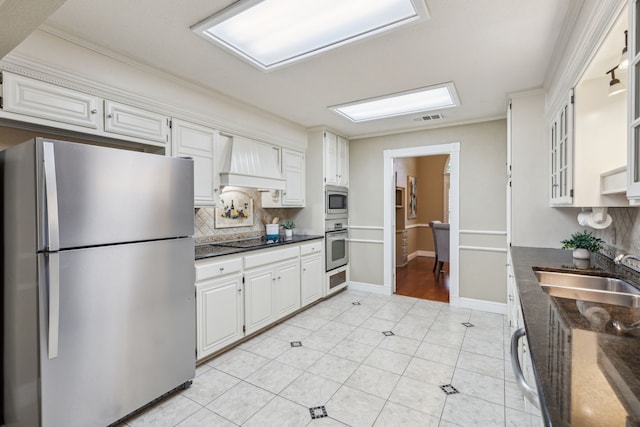 kitchen featuring stainless steel appliances, a sink, custom exhaust hood, tasteful backsplash, and white cabinetry