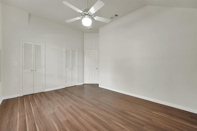 unfurnished bedroom featuring multiple closets, wood finished floors, vaulted ceiling, and baseboards