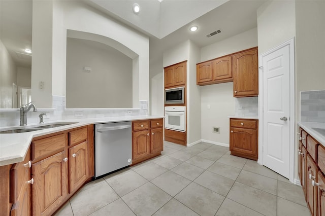 kitchen with appliances with stainless steel finishes, a sink, brown cabinets, light countertops, and recessed lighting