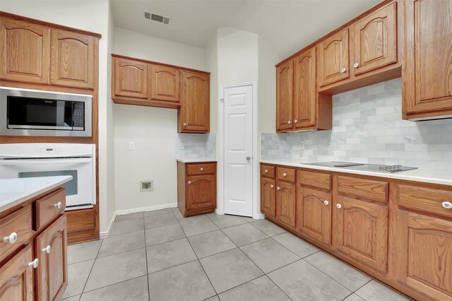 kitchen featuring white oven, black electric cooktop, stainless steel microwave, decorative backsplash, and brown cabinetry