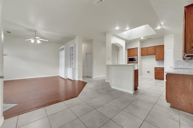 kitchen with stainless steel microwave, open floor plan, light countertops, lofted ceiling, and light tile patterned floors