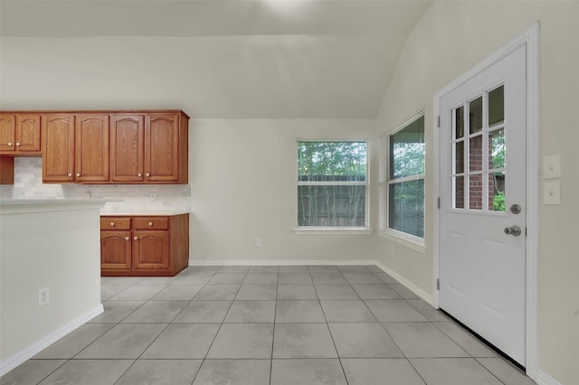 kitchen featuring light tile patterned flooring, light countertops, decorative backsplash, brown cabinets, and lofted ceiling