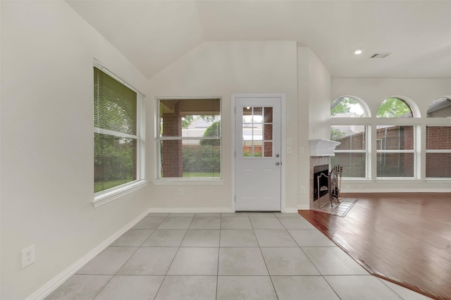 unfurnished living room featuring tile patterned flooring, lofted ceiling, a tile fireplace, and baseboards