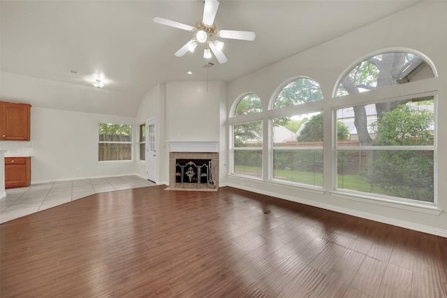 unfurnished living room featuring healthy amount of natural light, ceiling fan, a tiled fireplace, and baseboards
