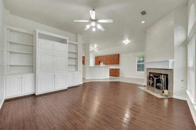 unfurnished living room with ceiling fan, wood finished floors, a tiled fireplace, and baseboards