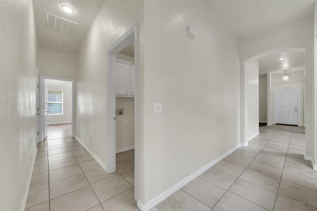 hall with arched walkways, light tile patterned flooring, and baseboards