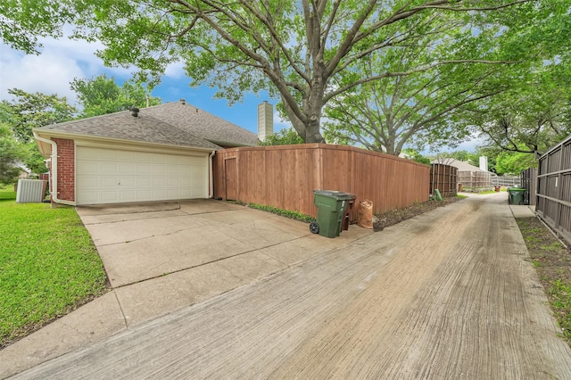 view of side of property featuring fence, driveway, brick siding, a shingled roof, and a gate