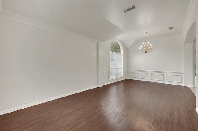 empty room with a chandelier, dark wood finished floors, lofted ceiling, wainscoting, and crown molding
