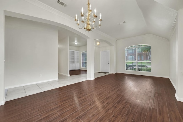 unfurnished living room with ornamental molding, arched walkways, wood finished floors, a chandelier, and baseboards