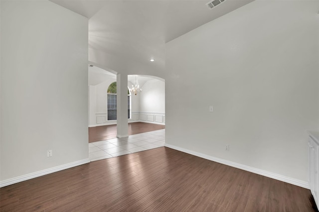 unfurnished room with arched walkways, a chandelier, wood finished floors, and baseboards