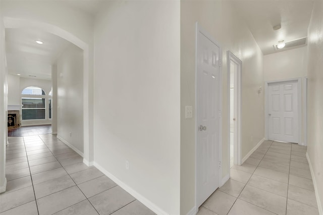 hallway with light tile patterned floors, arched walkways, and baseboards