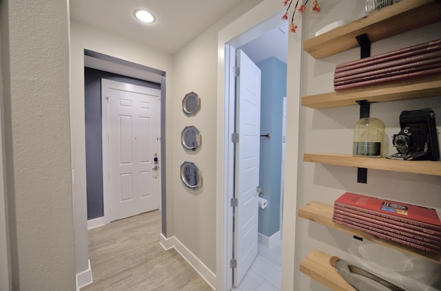 hall featuring baseboards, light wood-type flooring, and recessed lighting