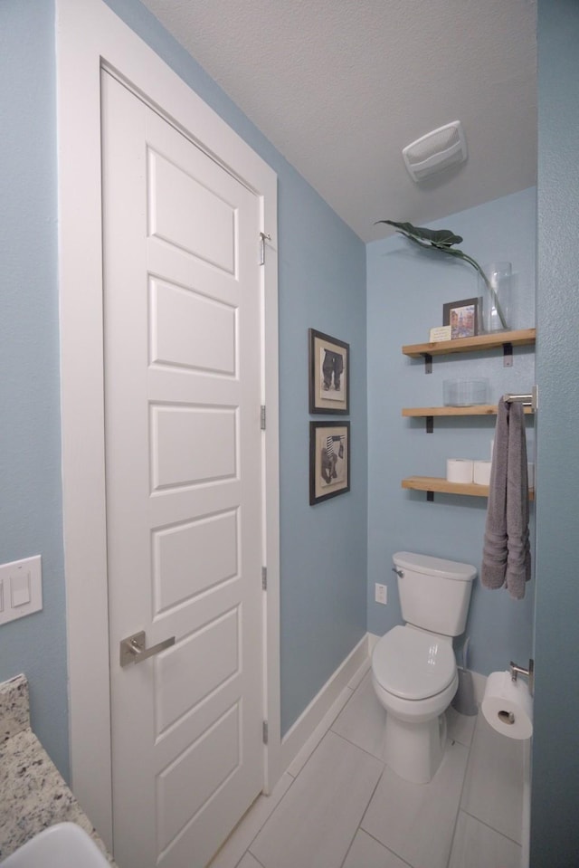 bathroom with toilet, baseboards, tile patterned floors, and a textured ceiling