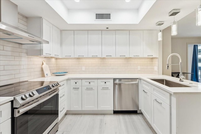 5909 Luther Ln Unit 1002, Dallas, TX 75225 - kitchen featuring stainless steel appliances, wall chimney exhaust hood, a sink, a peninsula, and a raised ceiling