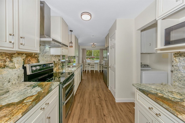 7616 Circle Dr, North Richland Hills, TX 76180 - kitchen featuring appliances with stainless steel finishes, washer / clothes dryer, wall chimney range hood, a sink, and light wood-style flooring