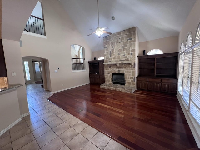 8205 Fountain Springs Dr, Plano, TX 75025 - unfurnished living room with a ceiling fan, a stone fireplace, arched walkways, tile patterned floors, and high vaulted ceiling