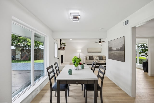 dining room featuring light wood finished floors, a fireplace, ceiling fan, and baseboards