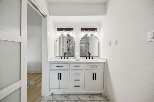 full bath with double vanity, marble finish flooring, baseboards, and a shower