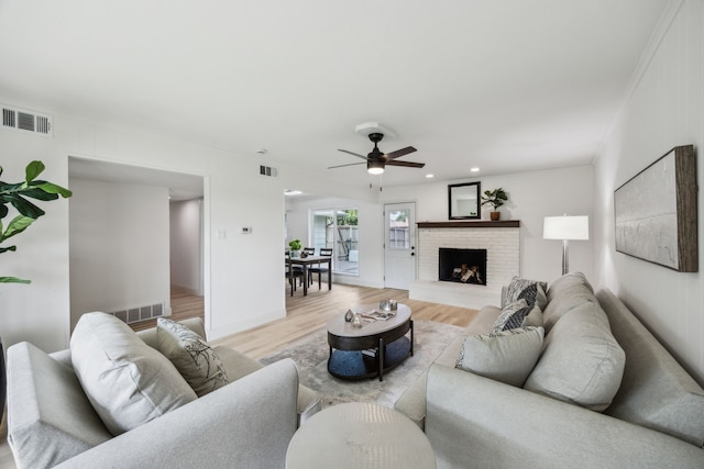 living area with wood finished floors, a ceiling fan, a brick fireplace, and recessed lighting