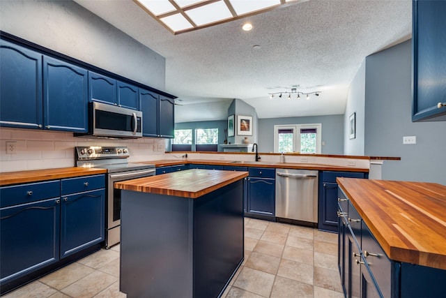 kitchen featuring wood counters, stainless steel appliances, blue cabinetry, a sink, and a peninsula