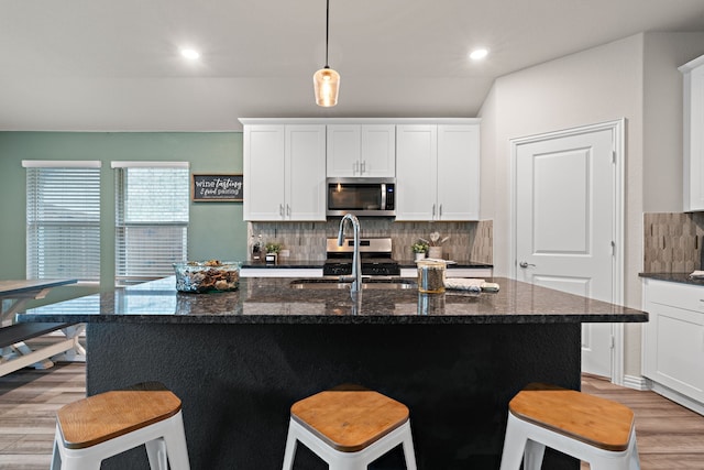 3112 Kingsgarden Rd, Denton, TX 76207 - kitchen featuring appliances with stainless steel finishes, a sink, light wood-style floors, decorative backsplash, and a kitchen bar