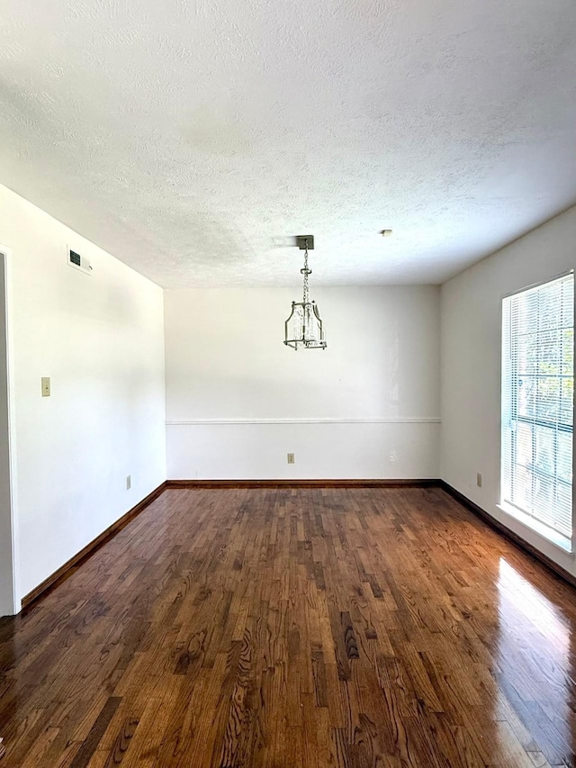 spare room featuring a textured ceiling, dark wood-style flooring, and baseboards