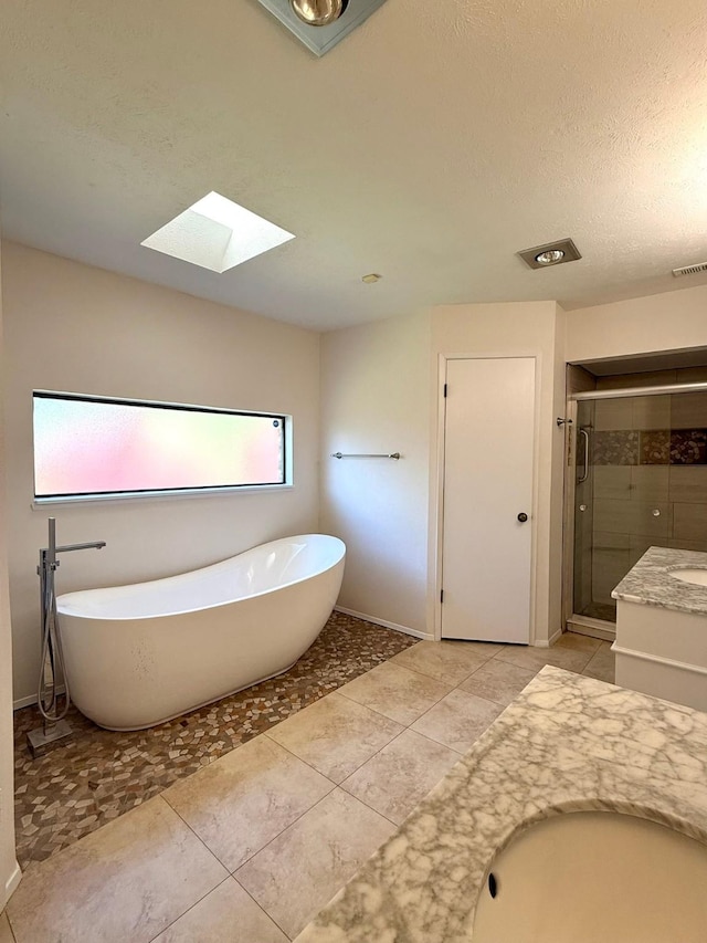 bathroom with a skylight, a shower stall, a freestanding bath, vanity, and a textured ceiling