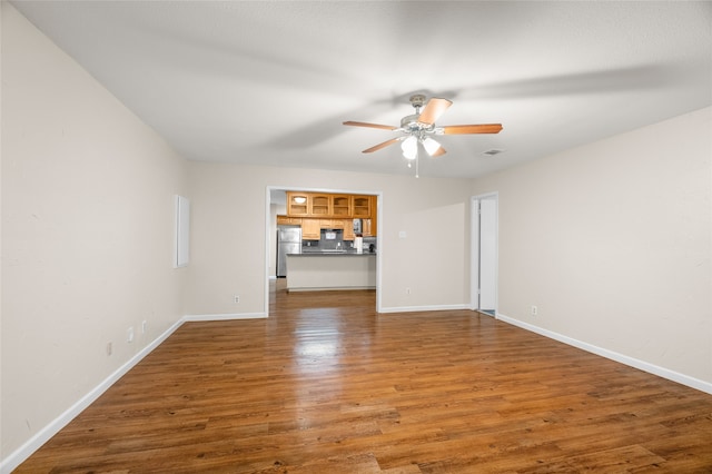 unfurnished living room with ceiling fan, wood finished floors, and baseboards
