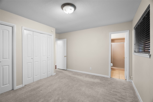unfurnished bedroom with carpet, a textured ceiling, connected bathroom, and baseboards