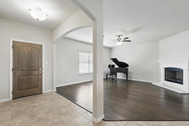 240 Springwood Ranch Loop, Springtown, TX 76082 - foyer entrance with arched walkways, a ceiling fan, a fireplace with raised hearth, light wood-type flooring, and baseboards