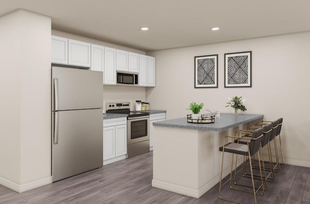 428 Garvin St, Eastland, TX 76448 - kitchen with appliances with stainless steel finishes, wood finished floors, white cabinets, a kitchen breakfast bar, and baseboards