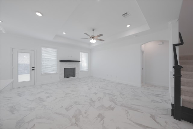 2301 Miramar Dr, Little Elm, TX 75068 - unfurnished living room featuring arched walkways, a raised ceiling, a ceiling fan, a stone fireplace, and stairs