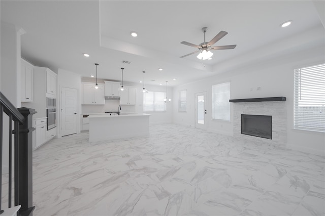 2301 Miramar Dr, Little Elm, TX 75068 - unfurnished living room featuring a raised ceiling, ceiling fan, a stone fireplace, recessed lighting, and a sink