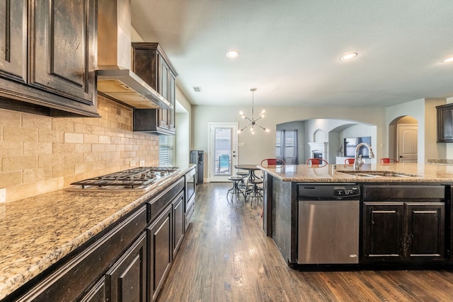 1005 Caudle Ln, Savannah, TX 76227 - kitchen with stainless steel appliances, wall chimney exhaust hood, arched walkways, a sink, and backsplash