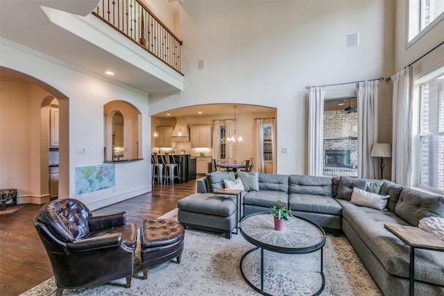 living room with dark wood-type flooring, arched walkways, a towering ceiling, healthy amount of natural light, and ornamental molding