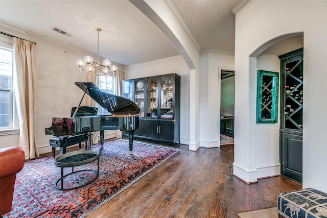 living area featuring wood finished floors, baseboards, ornamental molding, a chandelier, and arched walkways