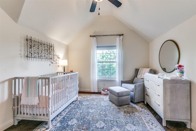 bedroom with a crib, vaulted ceiling, wood finished floors, ceiling fan, and baseboards