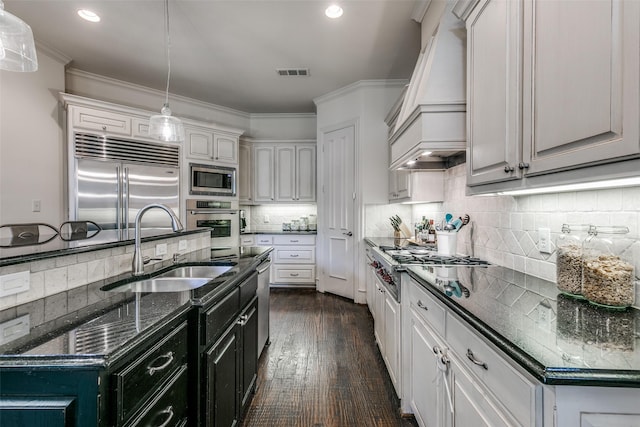kitchen with built in appliances, custom range hood, a sink, pendant lighting, and tasteful backsplash
