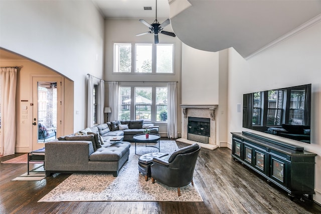 living area featuring a ceiling fan, a towering ceiling, wood finished floors, a high end fireplace, and crown molding