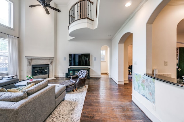 living room with arched walkways, dark wood-style floors, a ceiling fan, ornamental molding, and baseboards
