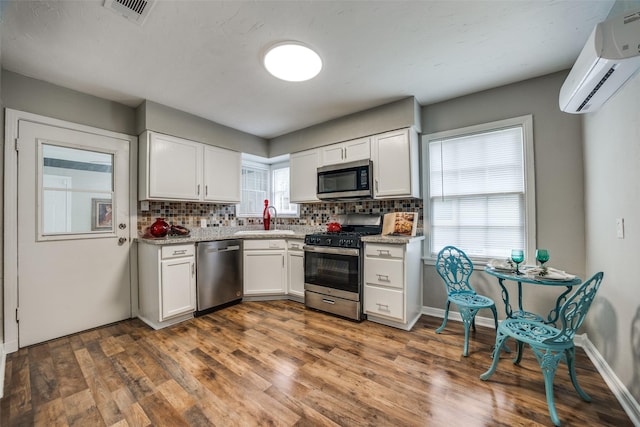 2614 Ivandell Ave, Dallas, TX 75211 - kitchen with appliances with stainless steel finishes, a sink, an AC wall unit, white cabinetry, and tasteful backsplash