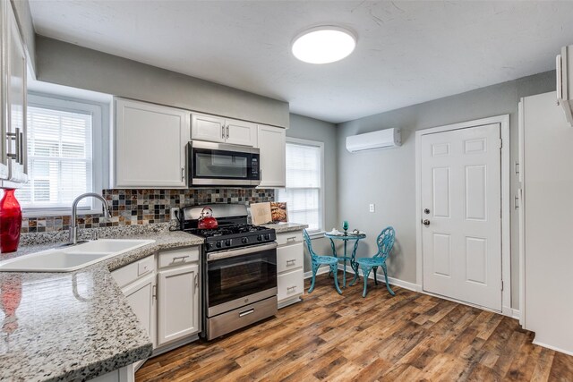 2614 Ivandell Ave, Dallas, TX 75211 - kitchen with appliances with stainless steel finishes, a sink, a wall mounted AC, backsplash, and white cabinetry