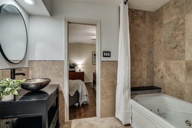 ensuite bathroom with tile walls, a combined bath / shower with jetted tub, and vanity