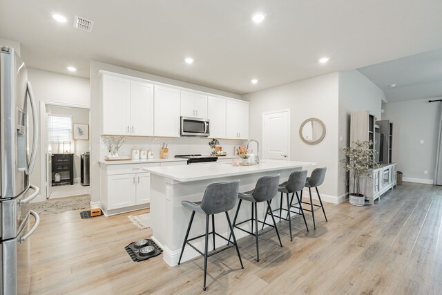 223 Quarry St, Melissa, TX 75454 - kitchen with appliances with stainless steel finishes, light wood-style flooring, a kitchen bar, backsplash, and an island with sink