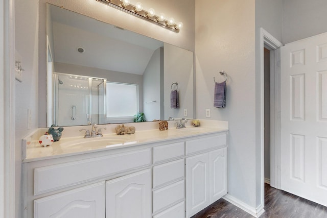 8614 Granville Dr, Dallas, TX 75249 - full bathroom featuring wood finished floors, a shower stall, double vanity, and vaulted ceiling