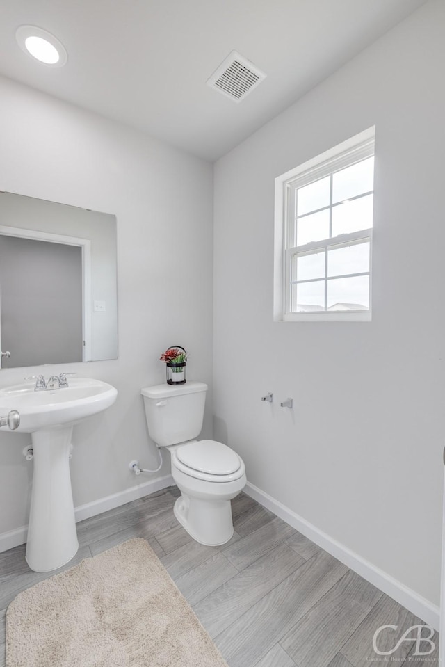 409 Garvin St, Eastland, TX 76448 - half bathroom featuring toilet, baseboards, wood finished floors, and a sink